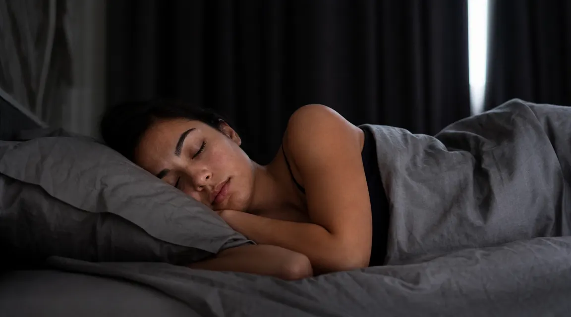 Woman sleeping peacefully in a dark bedroom with curtains drawn